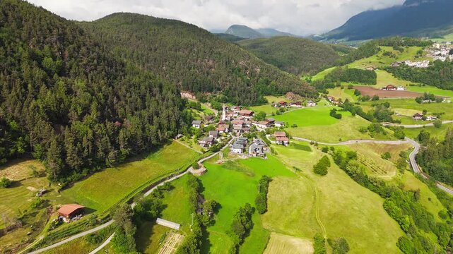 Drone footage of a small village beside mountain woodland in South Tyrol, Italy. Sunlit rural landscape in the Dolomite Alps
