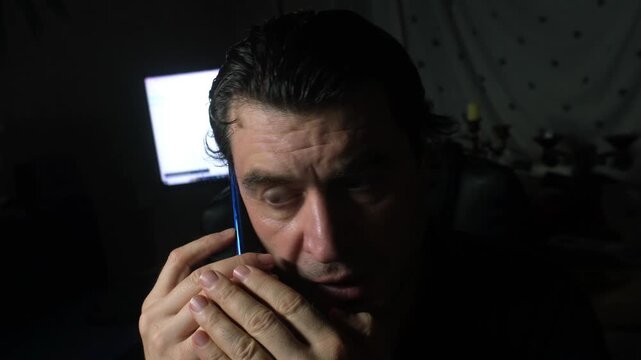 A man is talking on the phone, afraid of being overheard. He is frightened and glances around timidly.