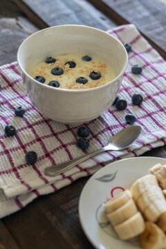 A delicious, healthy breakfast in a bowl with yogurt, oatmeal, and blueberries, alongside a plate of banana slices on a wooden table