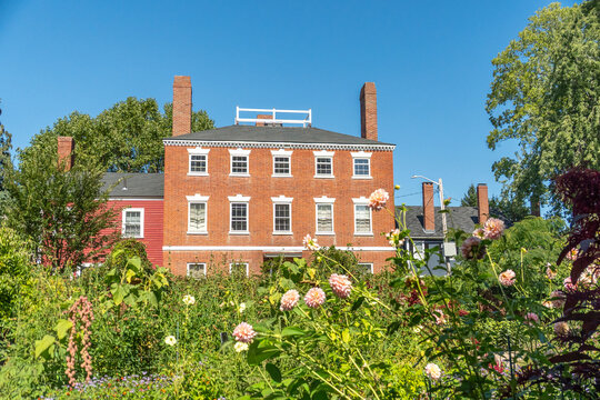 Brick townhouse in Salem Massachusetts with white trim under blue sky and blooming garden front yard