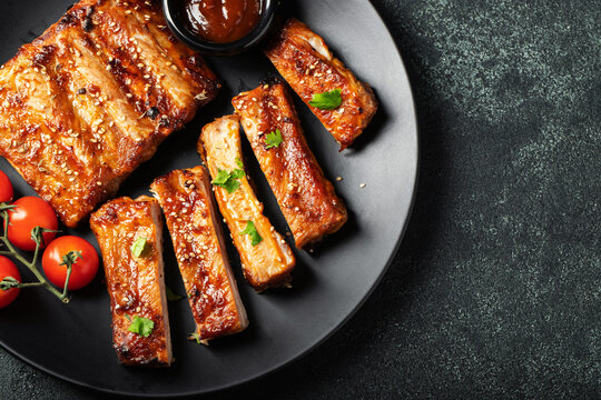 Hot grilled spare ribs from a summer BBQ served on a plate with sauce. Top view. Copy space