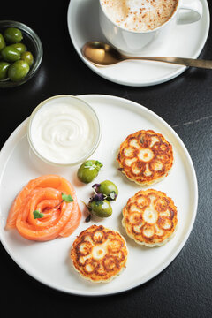 Savory Syrniki with Smoked Salmon, Olives and Sour Cream on White Plate