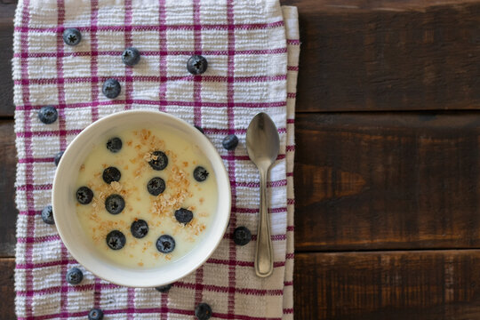 Aerial view of a bowl of yogurt, oatmeal, and blueberries on a tablecloth in rustic wooden table, ready to be served for breakfast or a healthy snack
