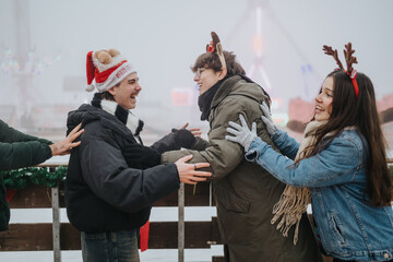 Naklejka premium Three friends wearing holiday headbands and winter coats laugh and embrace outdoors. They celebrate together at a festive winter market with cheerful expressions.