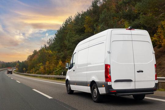 White courier delivery van drives highway autumn forest dramatic warm sunset sky. Logistics, transport and delivery concept blends motion, travel and seasonal landscape in calm rural scene