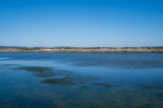 Calm blue waters of coastal salt marsh lagoon with rural village on horizon