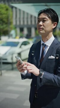 Businessman scrolling on his smartphone while waiting on a street in Tokyo