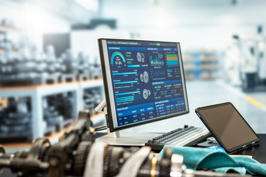 Computer monitor and tablet displaying production data beside machine parts in a modern factory workshop.