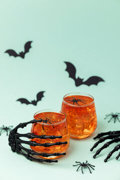 Skeleton hands hold Halloween drinks with spiders and bats on light blue background