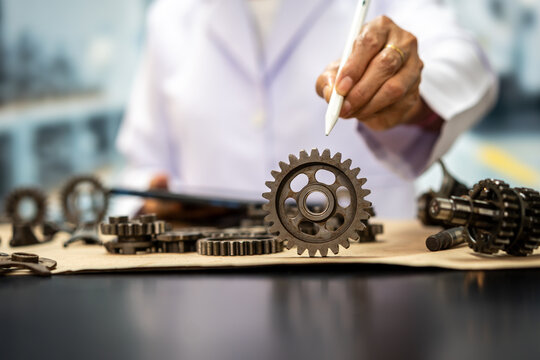 Close-up of a mechanic or engineer pointing at a metal gear on a workbench filled with machine parts, showing industrial repair, maintenance and manufacturing.