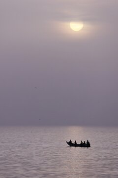Vue de loin, au lever du soleil, de la silhouette d'une barque de p&ecirc;cheurs sur une mer calme, avec un ciel rose mauve. C&ocirc;te du S&eacute;n&eacute;gal, un matin, au large de l'&icirc;le de Gor&eacute;e. 