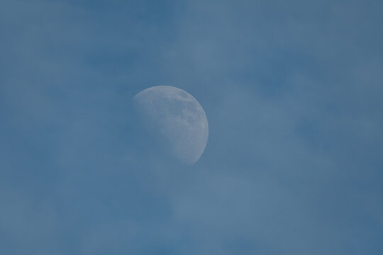 Half moon visible in pale blue sky with light clouds and copy space