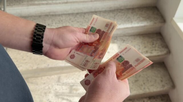 Man hands counting a large pack of five thousand rubles cash banknotes close up. This is a lot of paper money. Successful deal or loan payment process on the stairs. Financial budget wealth income. 