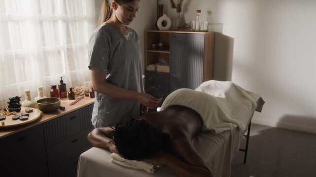 Caucasian young adult woman practitioner performing moxibustion therapy on African American young adult woman. Clip ideal for alternative medicine, acupuncture, and holistic spa promotions