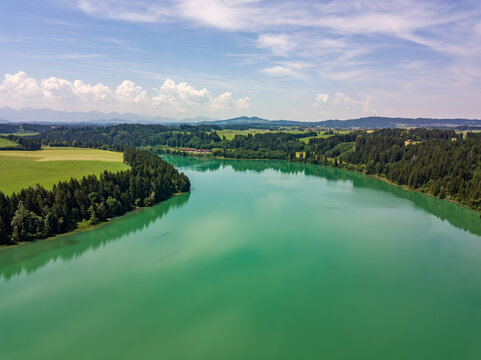 Aerial drone view of turquoise green Lech river surrounded by dense pine forests and Bavarian Alps in distance, German countryside river landscape concept