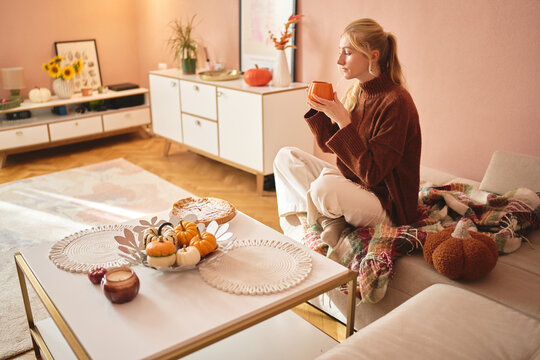Woman relaxing with a warm drink in an autumn living room.