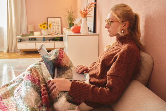 Woman working on laptop in cozy sunlit living room.