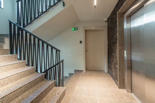 Modern Interior Hallway in Residential Building with Granite Staircase, Elevator, Black Railing and Entrance Door