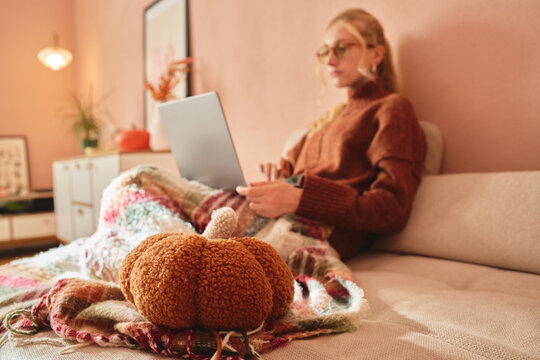 Woman working on laptop with blanket and plush pumpkin
