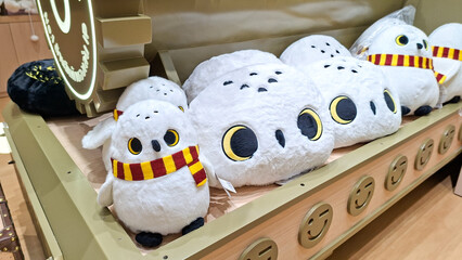 Obraz premium cute white hedwig snowy owl plush toy and cushion wearing scarf sitting on wooden display shelf on September 16, 2026 in Bangkok, Thailand.