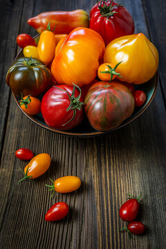 Assorted fresh heirloom tomatoes in a bowl on a rustic wooden background.