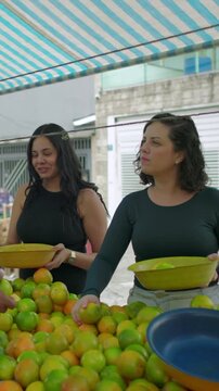 Hispanic vendor and friendly shoppers gathered around a fruit table choosing citrus together, sharing tips and easy back-and-forth decisions over fresh produce