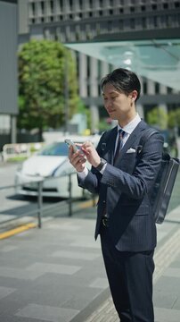 Businessman in a pinstripe suit checking his smartphone on a Tokyo sidewalk