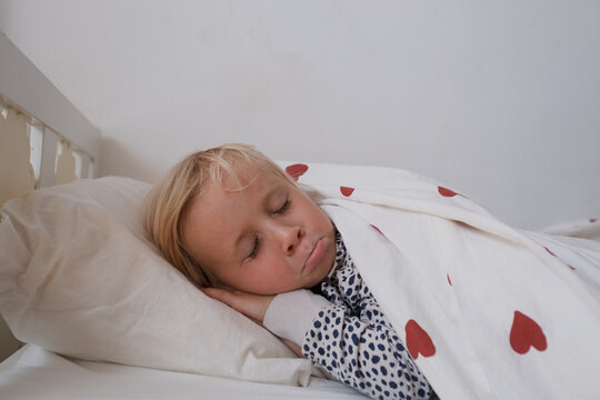  little girl sleeping peacefully in bed under duvet with red heart print
