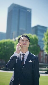 Smiling Japanese businessman on a phone call beside a green plaza in central Tokyo