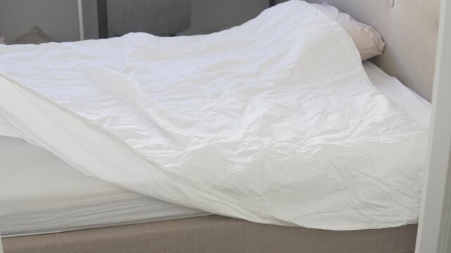 Woman spreading and arranging a clean white duvet on a bed while changing fresh bedding in a bright bedroom at home