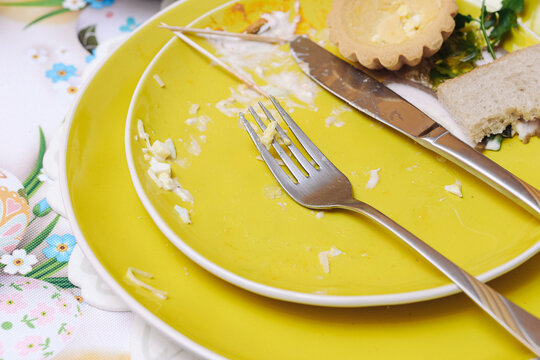 Used yellow plates with fork and knife after meal background. Leftover food and dirty tableware. Finished lunch setting. Empty dishes. Food waste and cleanup concept. Household routine. Daily cleanup.