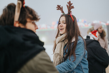 A teenage girl wearing reindeer antler headband and scarf talks with a friend at a winter event. © qunica.com