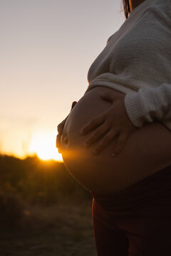 Pregnant belly cradled by hands at golden sunset outdoors, expectant mother in serene silhouette