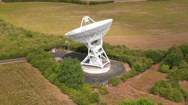 Aerial view of a massive white radio telescope dish for interstellar astronomy research surrounded by green fields in Cambridgeshire, UK