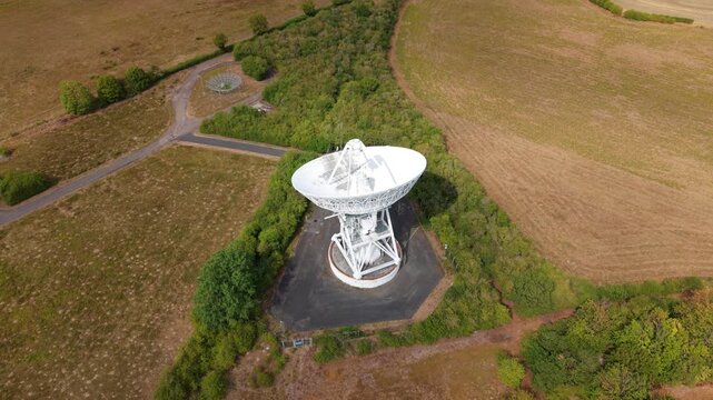 Aerial view of a massive white radio telescope dish for interstellar astronomy research surrounded by green fields in Cambridgeshire, UK