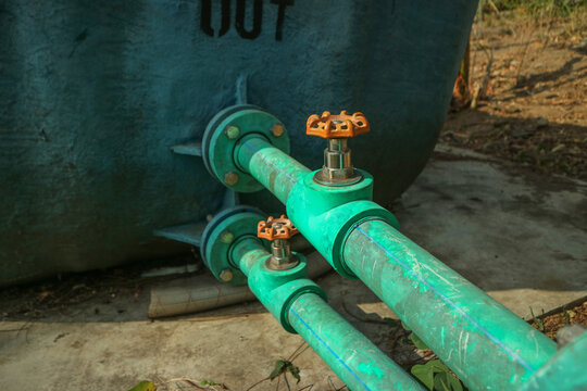Two green PVC water pipes featuring brass gate valves with orange handwheels on An outdoor industrial water distribution and plumbing setup.