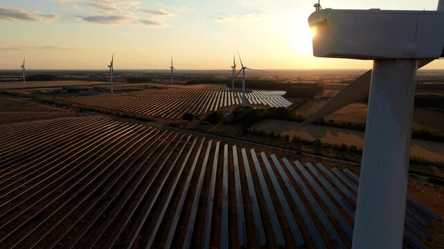 Hybrid solar farm and wind turbines at golden hour sunset in an aerial view in Chelveston, UK