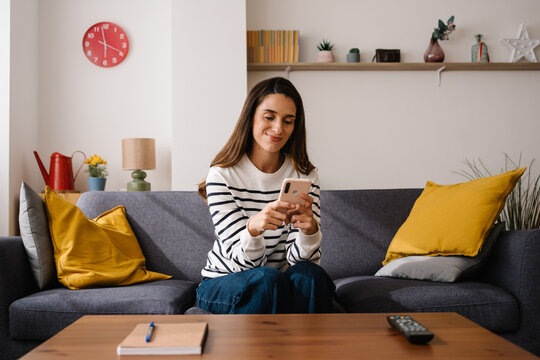 Casual woman on sofa texting on smartphone app in cozy living room relaxing at home