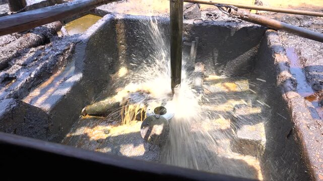 Close up of long metal bailer pipe extracting crude oil with splash at Wonocolo traditional oil well, Bojonegoro, East Java, Indonesia. Traditional petroleum extraction and heritage mining process.