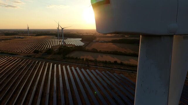 Aerial wide shot of hybrid solar and wind renewable energy farm glowing at golden hour sunset in Northampton UK