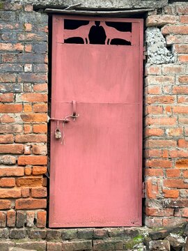 Vintage pink metal door locked with padlock on old rustic red brick wall vertical stock photo