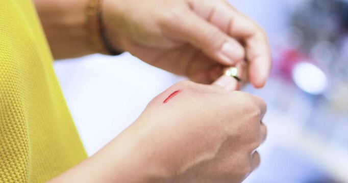 Woman testing red cosmetic color on the back of her hand and blending it with a finger to check shade and texture, beauty product testing and shopping, close-up