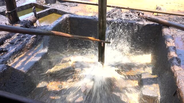 Close up of long metal bailer pipe extracting crude oil with splash at Wonocolo traditional oil well, Bojonegoro, East Java, Indonesia. Traditional petroleum extraction and heritage mining process.