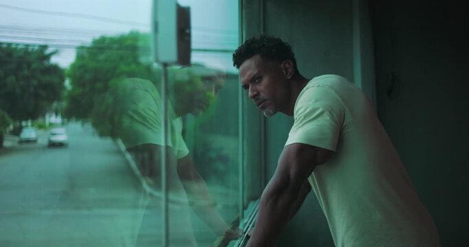 Man of African descent leaning on window, gazing outside with intense focus, deep contemplation, reflection visible in glass, introspective moment, urban solitude, quiet thoughts