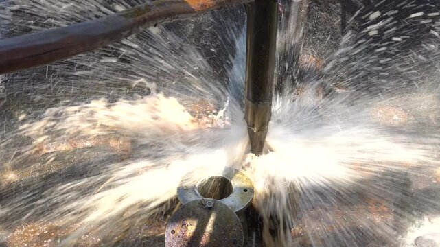 Close up of long metal bailer pipe extracting crude oil with splash at Wonocolo traditional oil well, Bojonegoro, East Java, Indonesia. Traditional petroleum extraction and heritage mining process.