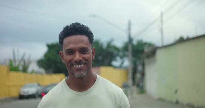 Man of African descent walking forward, smiling warmly at camera, friendly expression, positive energy, relaxed demeanor, urban street background, confident and approachable presence