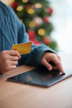 Woman holding credit card while browsing a tablet during Christmas, representing online shopping, digital payment, e-commerce purchases, holiday spending and seasonal retail at home.
