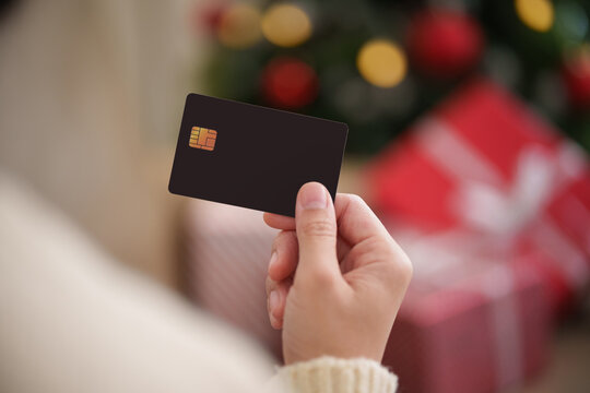Woman holding credit card with Christmas gifts and festive lights in the background, representing holiday shopping, seasonal spending, cashless payment, retail purchases and finance.