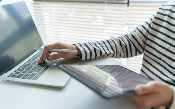Creative professional using digital tablet and laptop at a bright workspace, representing, productivity, freelance work and modern business.