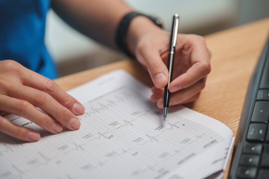 Doctor reviewing an ECG tracing with a pen at a desk, representing cardiology, heart rhythm analysis, cardiac diagnosis, patient monitoring and cardiovascular healthcare.